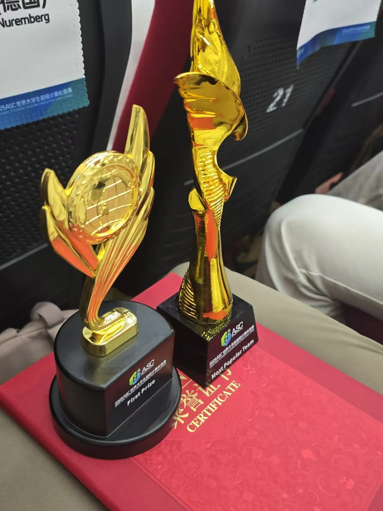 The First Prize and Most Popular Team trophies side by side on their certificates