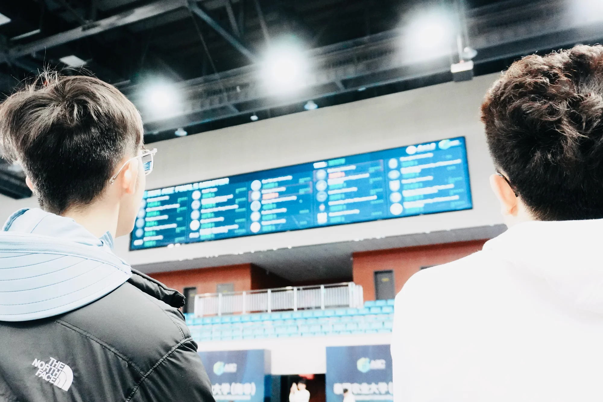 Two teammates, backs to the camera, watching the live leaderboard